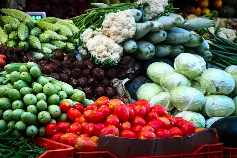 Tomates, repolhos, couves-flores e outras hortaliças empilhados em caixas de feira