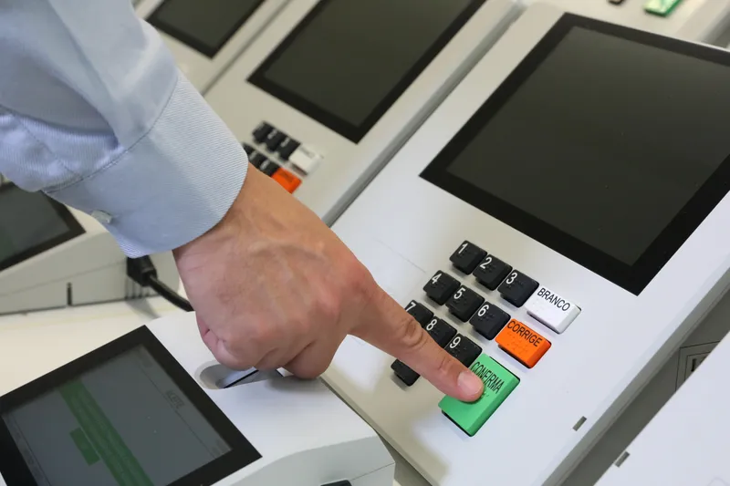 Mão aperta a tecla Confirma de uma urna eletrônica